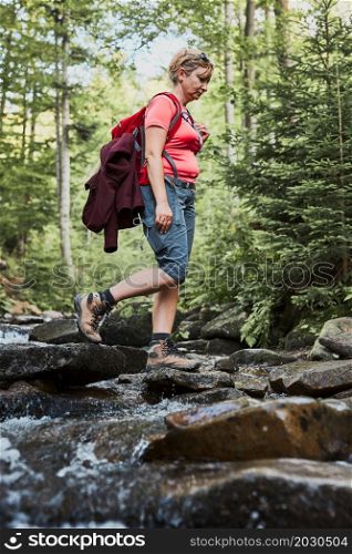 Woman with backpack hiking in mountains, spending summer vacation close to nature. Woman crossing the mountain stream
