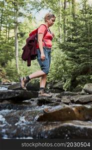 Woman with backpack hiking in mountains, spending summer vacation close to nature. Woman crossing the mountain stream
