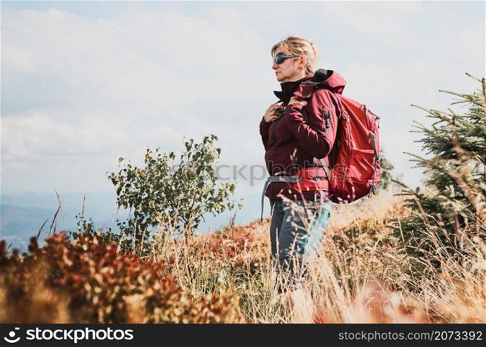 Woman with backpack hiking in mountains, spending summer vacation close to nature. Woman walking on path among bushes and grass