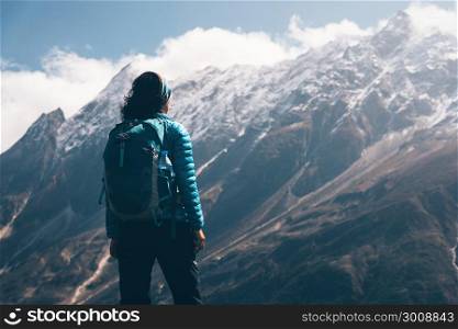 Woman with backpack looking on beautiful mountains in clouds at sunrise. Landscape with girl, high rocks with snowy peaks, blue sky with clouds in Nepal. Travel and tourism. Vintage style. Nature