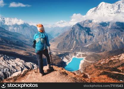 Woman with backpack on the mountain peak in autumn. Beautiful mountains in clouds, lake with azure water at sunset. Landscape with alone girl, snowy rocks, sky, glacier in Nepal. Travel in fall
