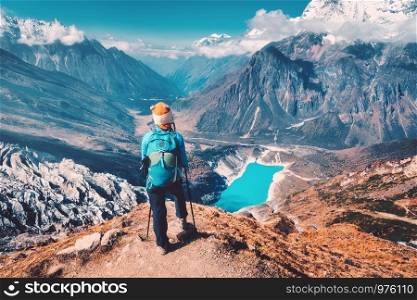 Woman with backpack on the mountain peak in autumn. Beautiful mountains in clouds, lake with azure water at sunset. Landscape with alone girl, snowy rocks, sky, glacier in Nepal. Travel in fall