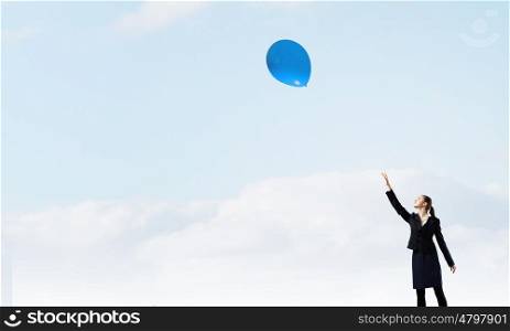 Woman with balloon. Young businesswoman reaching hand to touch balloon in sky