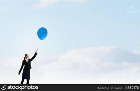 Woman with balloon. Young businesswoman reaching hand to touch balloon in sky