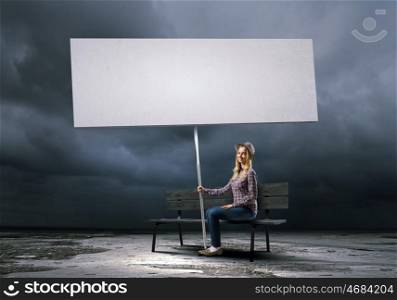 Woman with banner. Young girl in casual with white banner sitting on bench. Place for text
