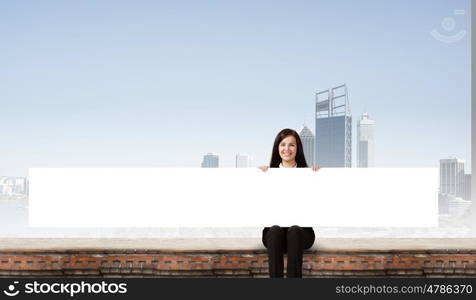 Woman with banner. Young woman sitting on top of building with blank banner