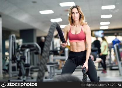 Woman with battle ropes exercise in the fitness gym. Young female wearing sportswear.