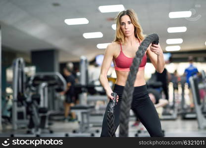 Woman with battle ropes exercise in the fitness gym. Young female wearing sportswear.