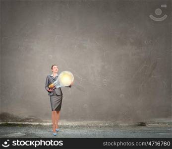 Woman with big bulb in hands. Young businesswoman carrying glass glowing light bulb in hands