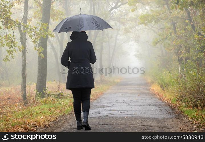 Woman with black umbrella and foggy forest