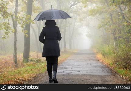 Woman with black umbrella and foggy forest