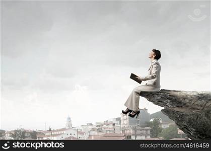 Woman with book. Adult woman in suit with old book in hand sitting on rock edge