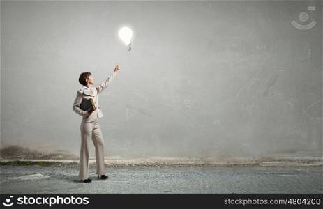 Woman with book. Adult woman in suit with old book in hand pointing at light bulb