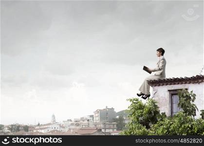 Woman with book. Adult woman in suit with old book in hand sitting on roof