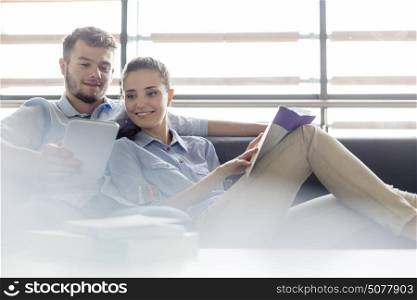 Woman with book using digital tablet on sofa at college