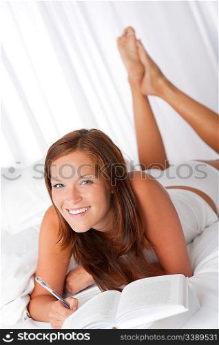 Woman with book writing notes and lying on white bed