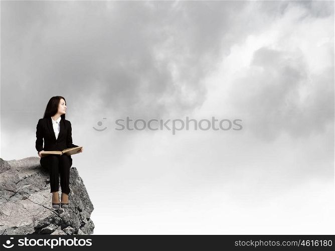 Woman with book. Young businesswoman sitting on rock edge with book in hands