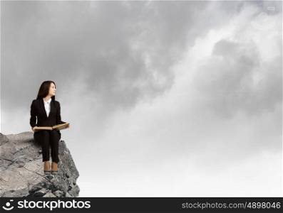 Woman with book. Young businesswoman sitting on rock edge with book in hands
