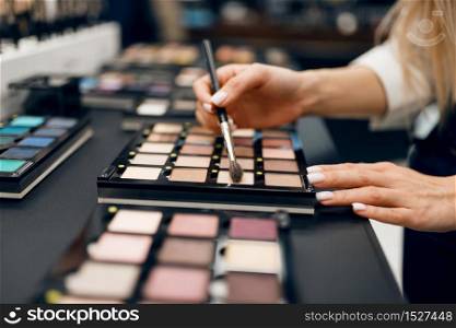 Woman with brush choosing shadows in cosmetics store. Buyer in luxury beauty shop salon, female customer in fashion market. Woman with brush choosing shadows, cosmetics store