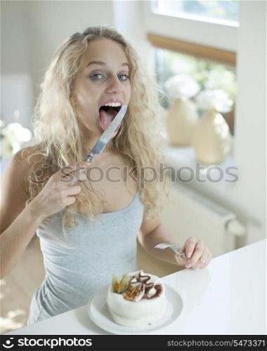 Woman with cake licking table knife at counter in house