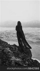 Woman with cape ofχffon on rock monochrome scenic photography. Picture of person with old glacier on background. High quality wallpaper. Photo concept for ads, travel blog, magazi≠, artic≤. Woman with cape ofχffon on rock monochrome scenic photography