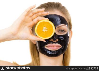 Woman with carbo detox black peel-off mask on face holding orange fruit. Teen girl taking care of oily skin, cleaning the pores. Beauty treatment. Skincare.. Girl black carbo mask on face holds orange fruit