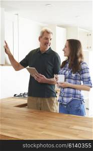 Woman With Carpenter Looking At Plans For Kitchen On Digital Tablet