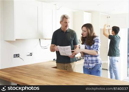 Woman With Carpenter Looking At Plans For New Kitchen
