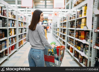 Woman with cart in supermarket, alcohol drinks department, family shopping. Female customer choosing alcoholic beverages in shop, buyers in market