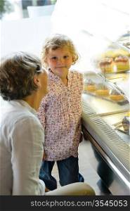 Woman with child girl in bakery choose cake grandmother and granddaughter