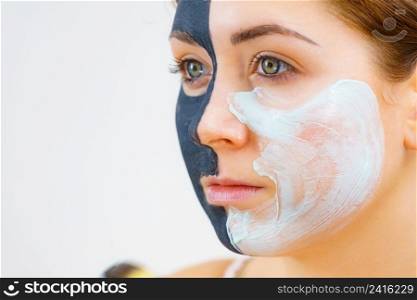 Woman with clay carbo black mask on half face applying white mud to clean skin. Girl taking care of oily complexion. Beauty procedures. Skincare.. Girl black mask on half face apply white mud