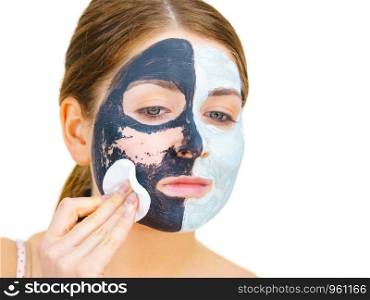 Woman with clay carbo black mask on one half face and white mud on second half. Girl removing cosmetic scrab with cotton swab. Female taking care of oily complexion. Skincare.. Girl remove black white mud mask from face