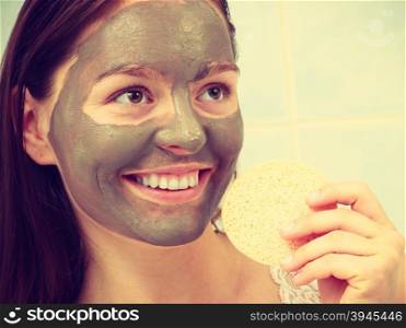 woman with clay mask in bathroom holds sponge to remove mud. Beauty procedures spa and skin care concept. Young woman with facial clay mask in bathroom holds sponge to remove mud filtered photo