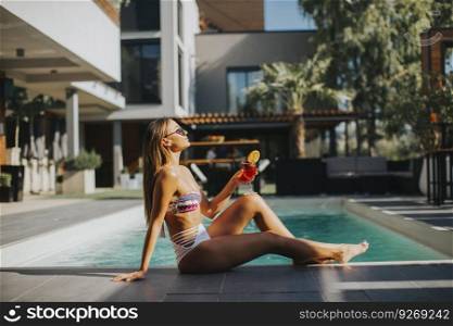 Woman with coctail posing by the pool at sunny day