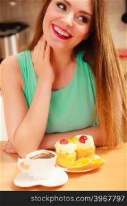 Woman with coffee cup cupcake in kitchen. Woman with cup of coffee and delicious gourmet sweet cream cake cupcake and orange. Lovely girl sitting in kitchen with hot beverage having breakfast. Appetite and gluttony concept.