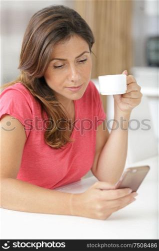 woman with coffee cup using mobile phone in home