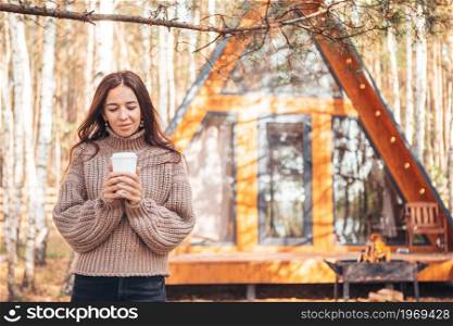 Woman with coffee enjoying autumn day background of her house. Beautiful girl walking at autumn warm day