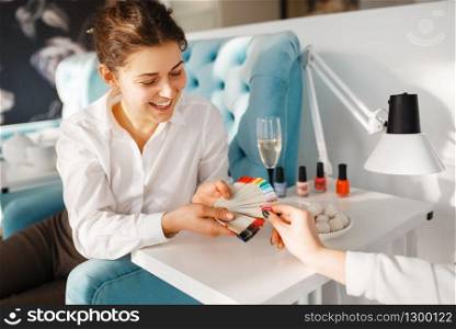Woman with color palette choosing nail varnish in beauty salon, manicure and pedicure procedure. Professional beautician service, female customer, toenail and fingernail care in spa studio