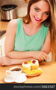 Woman with cup of coffee and delicious gourmet sweet cream cake cupcake and orange. Glutton girl sitting in kitchen with hot beverage having breakfast. Appetite and gluttony concept.. Woman with coffee and cake in kitchen. Gluttony.