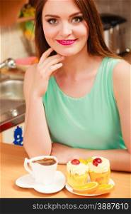 Woman with cup of coffee and delicious gourmet sweet cream cake cupcake and orange. Glutton girl sitting in kitchen with hot beverage having breakfast. Appetite and gluttony concept.. Woman with coffee and cake in kitchen. Gluttony.