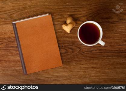 woman with cup of tea, cookies and book on wooden table