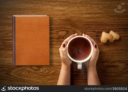 woman with cup of tea, cookies and book on wooden table