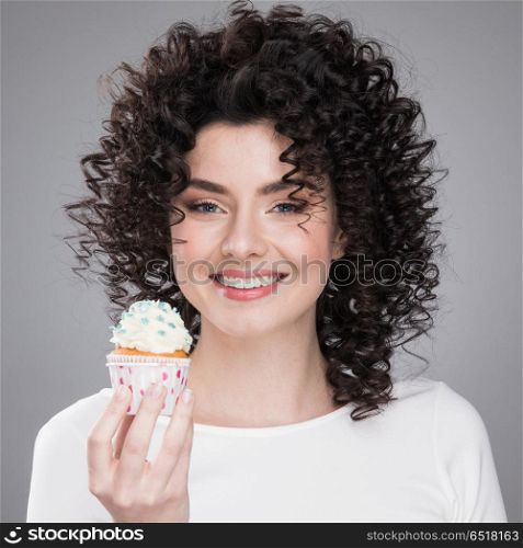 Woman with cupcake. Happy cute lovely curly young woman with curly hair holding cupcake and smiling