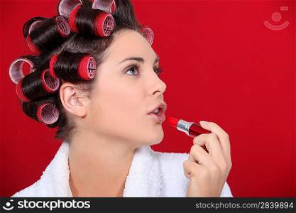 woman with curlers in her hair putting lipstick