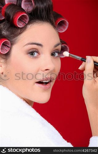 woman with curlers in her hair putting make up