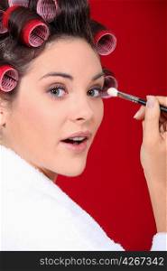 woman with curlers in her hair putting make up