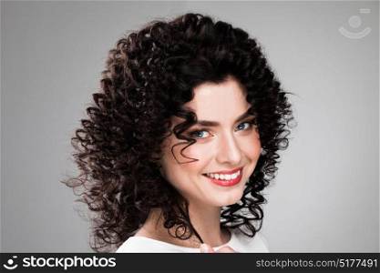 Woman with curly hair. Studio portrait of beautiful smiling woman with curly dark hair on gray background