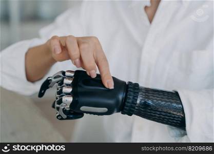 Woman with disability showing artificial robotic hand, switching changing the grip on her bionic prosthesis, close-up. Disabled person using myoelectric prosthetic arm with kinesthetic interface.. Woman with disability turns on high tech prosthetic arm, showing bionic prosthesis, close-up