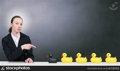 Woman with duck toy. Young businesswoman pointing with finger at yellow rubber duck toy on table