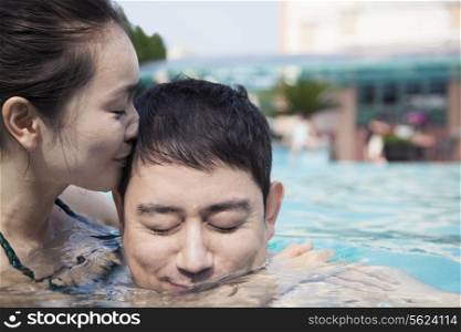 Woman with eyes closed kissing man on the cheek in the water in the pool